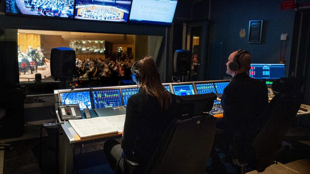 KOntrollrummet för radiosödningar i Berwaldhallen. Två bildproducener tittar ut mot orkestern som spelar på scenen.