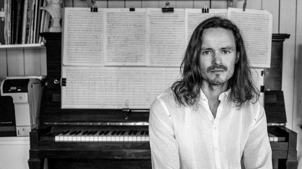 Ett svartvitt foto på Matthew Peterson framför ett piano och noter.